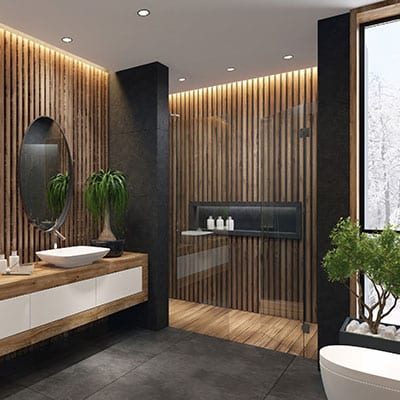 Modern bathroom with wood slat walls, a floating vanity with a round mirror, a vessel sink, and potted plants. A glass shower enclosure features matching wood slats and built-in shelving. Large window lets in natural light.