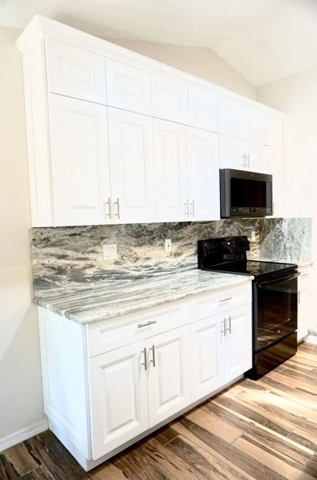 A modern kitchen features white cabinets, a gray and white marble countertop and backsplash, a black stove and microwave, and wood-patterned flooring.