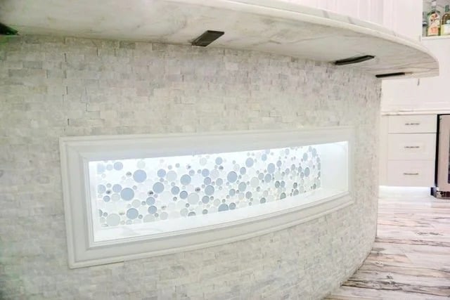 A light stone kitchen island features a rectangular window with a white frame, revealing a decorative glass panel filled with variously sized blue and clear bubbles. The kitchen floor and cabinets are visible in the background.