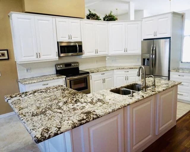 Modern kitchen with white cabinets, stainless steel appliances, and granite countertops. The large island features a double sink and a faucet, with wood and tile flooring throughout the space.
