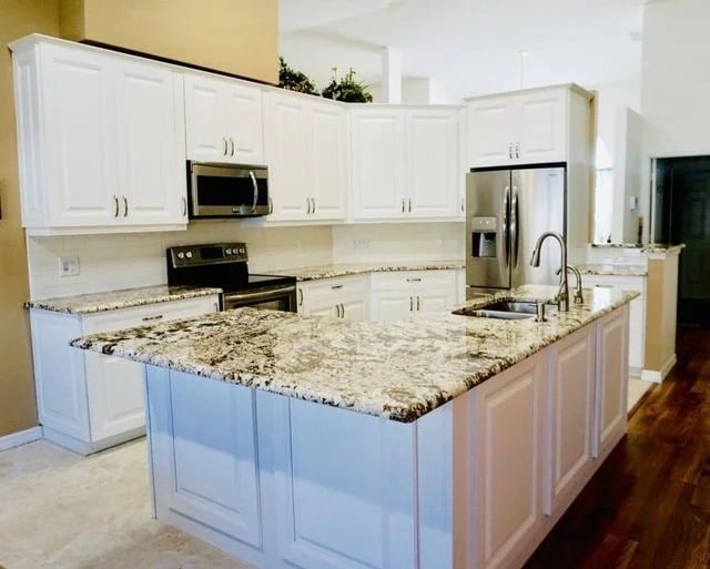 Modern kitchen with white cabinets, stainless steel appliances, and a large island featuring a marble countertop. The room has wood floors and neutral-colored walls, creating a clean and spacious look.