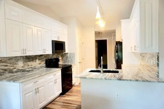 A modern kitchen with white cabinets, marble countertops and backsplash, black appliances, a built-in microwave, and wood-style flooring. Pendant lights hang above the sink on a peninsula counter.