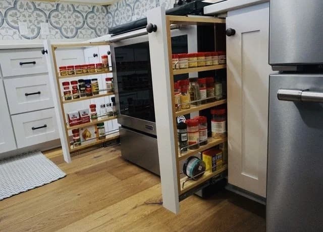 A kitchen with two pull-out spice racks built into the cabinets on either side of an oven, containing organized spice jars and cans. The racks are extended, showing their contents.