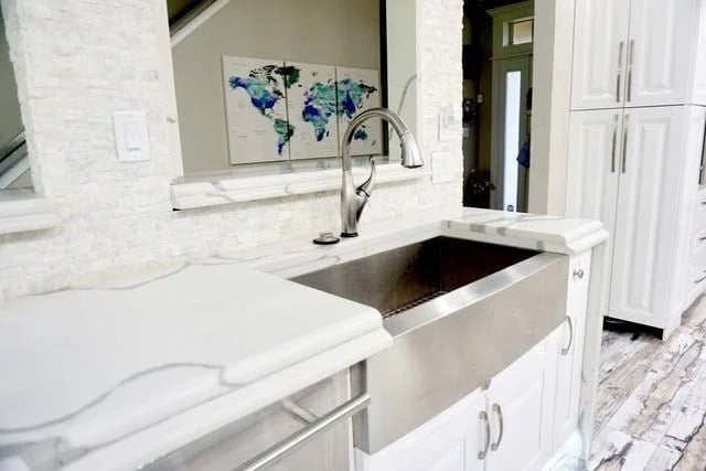 A modern kitchen sink with a stainless steel farmhouse basin, white cabinets, a tiled backsplash, and a gooseneck faucet; a world map artwork is visible in the background.