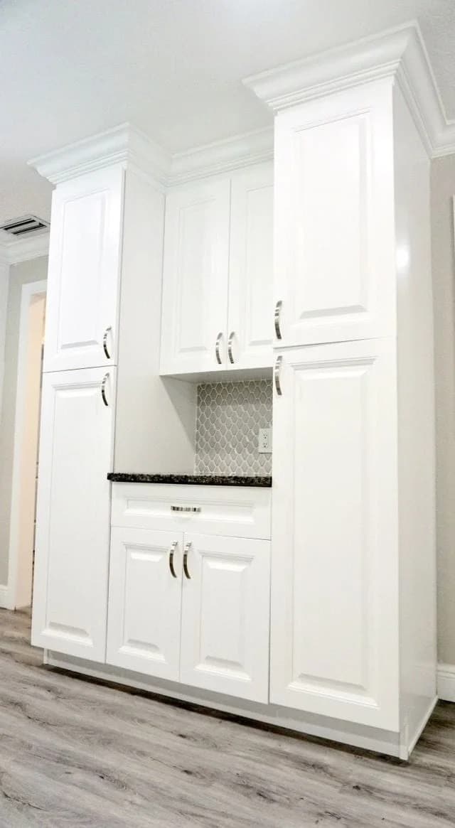 Tall white kitchen cabinets with silver handles, a black countertop, and a small gray and white tile backsplash. The cabinets are set against a light-colored wall and floor.