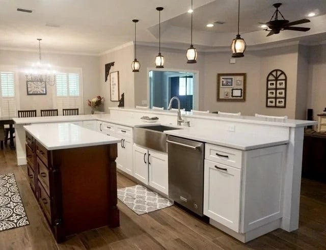 Spacious modern kitchen with white cabinets, stainless steel appliances, a farmhouse sink, and pendant lights above a large island with a wooden base. Dining area visible in the background.